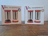Two new boxed V.F.P. Co salt and pepper sets, each with glass and stainless steel components and red lids and bases.