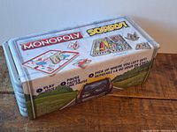 Side view of hinged metal case showing Monopoly and Sorry game logos with instructions for pausing and resuming games