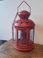 Front view of the red lantern with swag chain, showing the star cutouts and cylindrical candle holder inside.