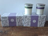 Two boxes of 100% natural scented candles with two candles on top of boxes showing glass jars and lids.