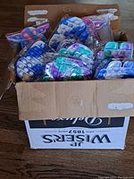 Top view of cardboard box filled with multiple plastic-wrapped fidget poppers in various shapes and colors