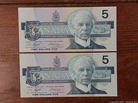 Front view of two Canadian five dollar bills, showing the portrait of Sir Wilfrid Laurier and denomination 5.