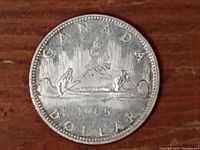 Front side of coin dated 1965 showing the iconic Voyageur and canoe design with the word CANADA and DOLLAR around the rim.