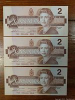 Front side of three 1986 Canadian two dollar bills showing Queen Elizabeth II portrait and denomination.