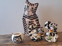 Overall view of the four ceramic cat-themed containers on a wooden surface against a light background. The items include a tall cat patterned vase, two cat salt and pepper shakers, and a small toothpick holder shaped like a cat face filled with toothpicks.
