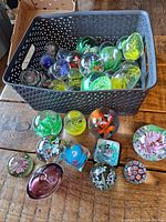 Paperweight lot in a black basket on a wooden surface with some paperweights laid out