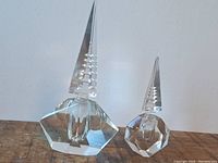 Two crystal perfume bottles on wooden surface, one larger and one smaller with detailed faceted stoppers and bases.