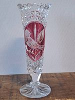 Full frontal view of a clear cut crystal vase with cranberry colored oval inset featuring a detailed bird design.