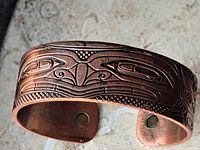 Close-up of copper bracelet showing detailed indigenous artwork of a grizzly bear with etched geometric patterns.