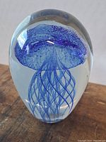 Front angle view of the oval glass paperweight showing the blue jellyfish inset inside the clear glass with detailed tentacles and bubbles.