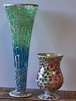 Tall mosaic vase and shorter mosaic vase side by side on wooden box against a wall