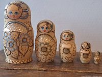 Five beige nested dolls hand-painted with blue and gold floral designs and dots, lined up by size.