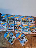 Full view of 12 unopened Hot Wheels cars in their original blue blister card packaging laid out on a flat surface.