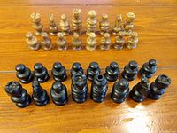 Complete set of brown and black onyx chess pieces arranged in two rows on a wooden table, showing all 32 pieces including kings, queens, bishops, knights, rooks, and pawns.