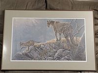 Framed print showing two mountain lions on rocky landscape with trees in background.