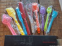 Nine silicone kitchen utensils individually wrapped in plastic, displayed on a wooden surface.