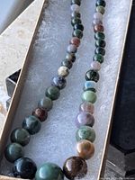 Close-up photo of the stone bead necklace showing various colors and sizes of beads on a soft cushioned display.