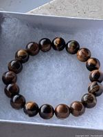 Top view of the bracelet showing polished Tiger's Eye beads with their distinctive golden and brown striped chatoyancy, placed inside a jewelry box with soft padding.