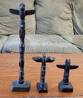 Three black totem poles of varying heights displayed on a wooden surface in front of a couch.