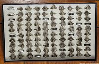 Tray holding 100 light metal rings with various intricate designs and sizes arranged in a grid.