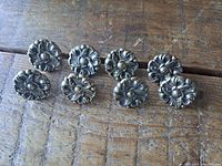 Eight vintage brass drawer knobs arranged on a wooden surface showing the floral pattern on the front.