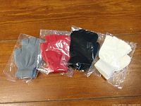 Four pairs of fingerless gloves in grey, red, black, and white, new and individually packaged.