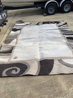 Full view of the brown and white geometric patterned area rug laid flat on concrete surface showing design and condition.