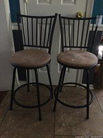 Pair of black metal frame swivel barstools with tall slatted backs and round tan seats shown front view