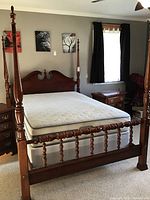 Four poster wooden bed frame with mattress, shown fully assembled in a carpeted room.