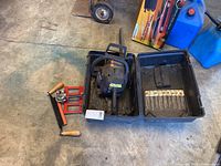 Photo showing Poulan chainsaw inside its black carrying case placed on concrete floor, with red and black bark remover tool beside it.
