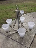 Chandelier resting on a concrete surface showing the full fixture with five frosted glass shades and metal arms in brushed finish.