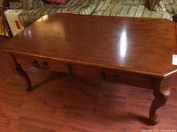 Full view of a rectangular wooden coffee table with a polished brown finish, showing two drawers with metal handles and curved legs.