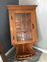 Full view of wooden corner wall cabinet with glass door and open bottom shelf