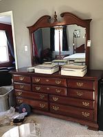 Front view of dark wood Dixie dresser with arched mirror and brass handles, some scratches visible.