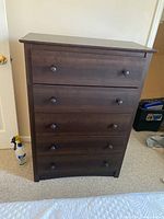 Front view of wood dresser with four drawers and round knobs, positioned on carpeted floor against wall.