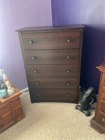 Frontal view of five-drawer wood dresser with matching round pulls and dark finish in a room with purple walls.