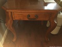 Front view of one wooden end table showcasing top surface, drawer with metal handle, and curved legs.