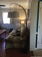 Full height view of floor lamp next to couch, showing the three curved arms and fabric lampshades.