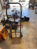 Front view of metal hand truck with visible wear and rust on frame and base plate.