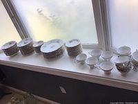 Full view of various stacked plates and cups near window, showing quantity and arrangement