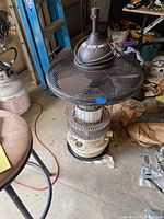 Dyna Glo kerosene heater with metal cage and glass reservoir visible, positioned under an Allen & Roth outdoor ceiling fan with metal guards and fan blades.