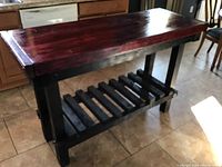 Front perspective of the kitchen island showing the dark reddish-brown polished wooden top and black frame with slatted lower shelf.