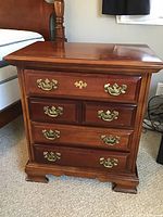 Front view of one Dixie wooden nightstand showing four drawers, brass handles, and wood finish.