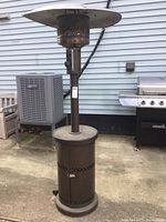 Full view of brown propane patio heater showing entire structure with bent top reflector and cylindrical body.