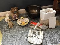 Photo showing all lot items spread on fabric, including the Gorham silverplate bowl, a yellow floral candy dish, dog and dove porcelain figures, a framed floral picture, and a box containing spoons.