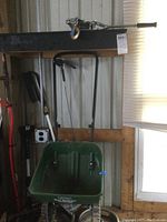 Photo showing the Scotts Turf Builder green push lawn spreader with handle and wheels leaning against wall.