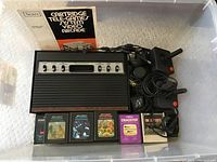 Full view of Sears Atari Tele-Games system including console, two joystick controllers, power adapter, instruction manual, and five game cartridges.