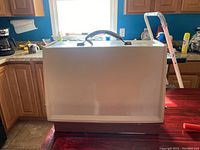 Off-white plastic carrying case with a black handle, placed on a kitchen counter with cabinets and window in the background.