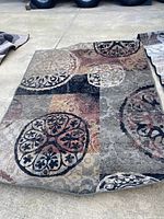 Rectangular rug showing an abstract circular pattern with colors gray, black, cream, and muted red on a concrete floor.