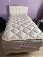 Twin bed with white faux leather button tufted headboard, Serta mattress, and metal bed frame setup in bedroom.